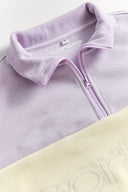 Close-up of a lilac quarter zip jumper with a brand logo on a white background
