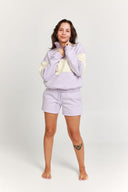 Woman wearing a light purple quarter zip jumper and shorts set on a white background