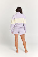 Person wearing a light purple and yellow striped quarter zip jumper with matching shorts on a white background