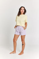 Woman wearing a yellow t-shirt and light purple shorts on a white background