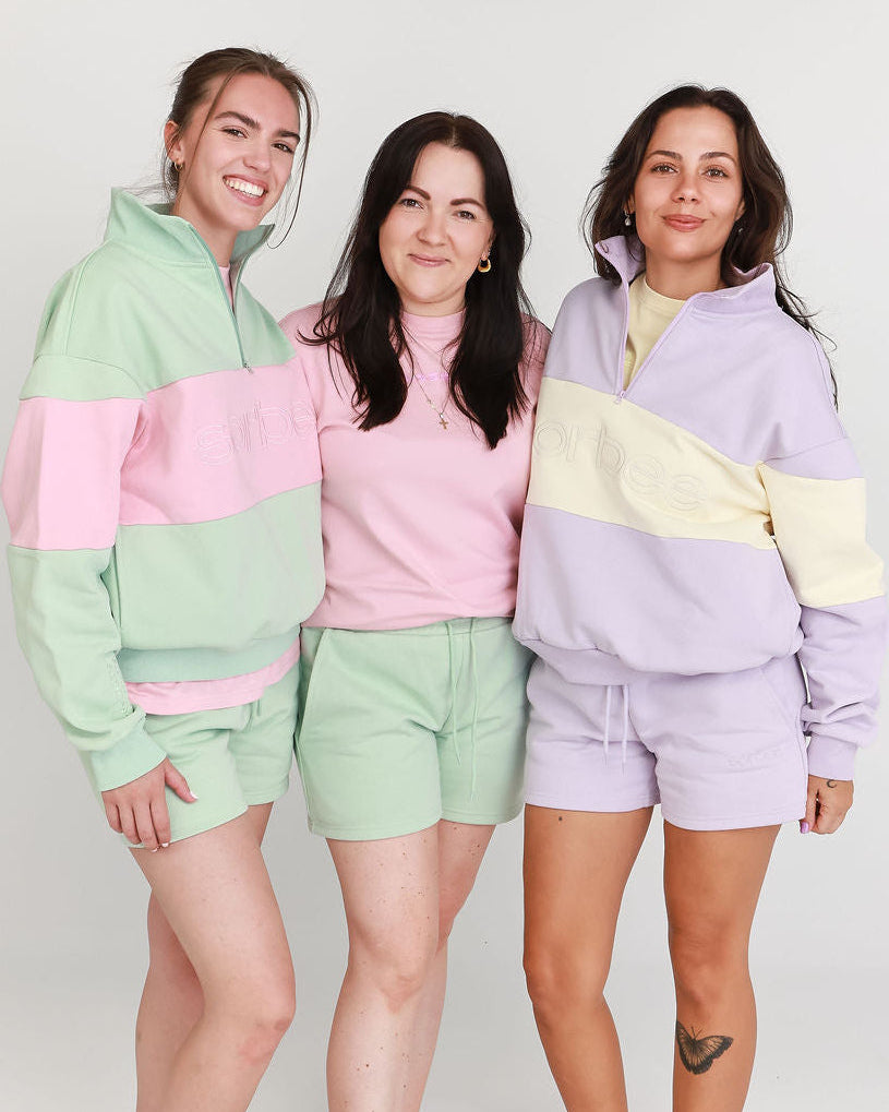 Three women wearing pastel color block outfits on a white background