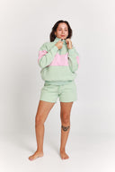 Person wearing a light green and pink quarter zip jumper and shorts set on a white background