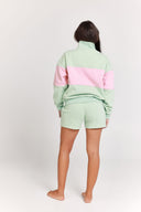 Person wearing a light green and pink striped quarter zip jumper and shorts set on a white background