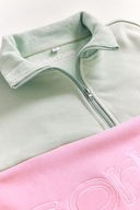 Light green and pink quarter zip jumper with branding on a white background